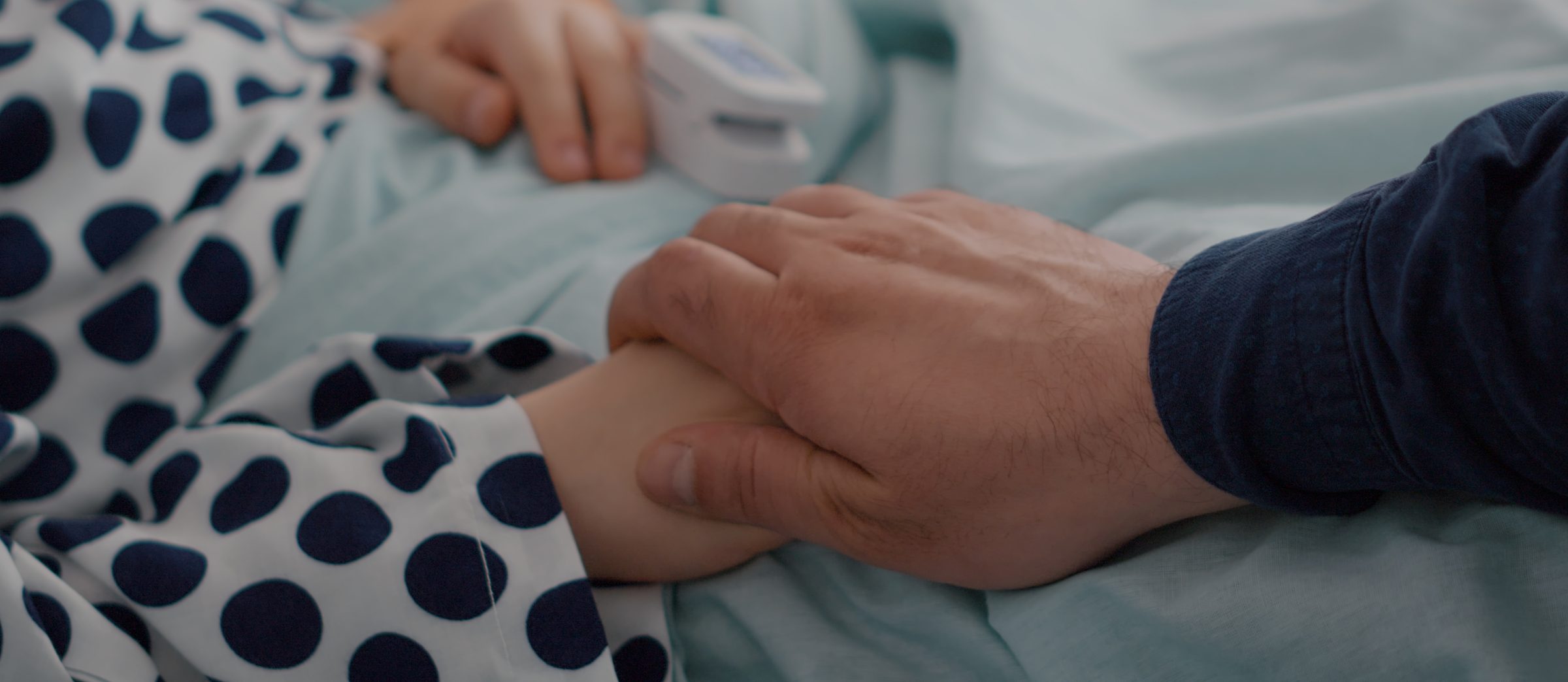 An adult holding the hand of a child resting in a hospital bed