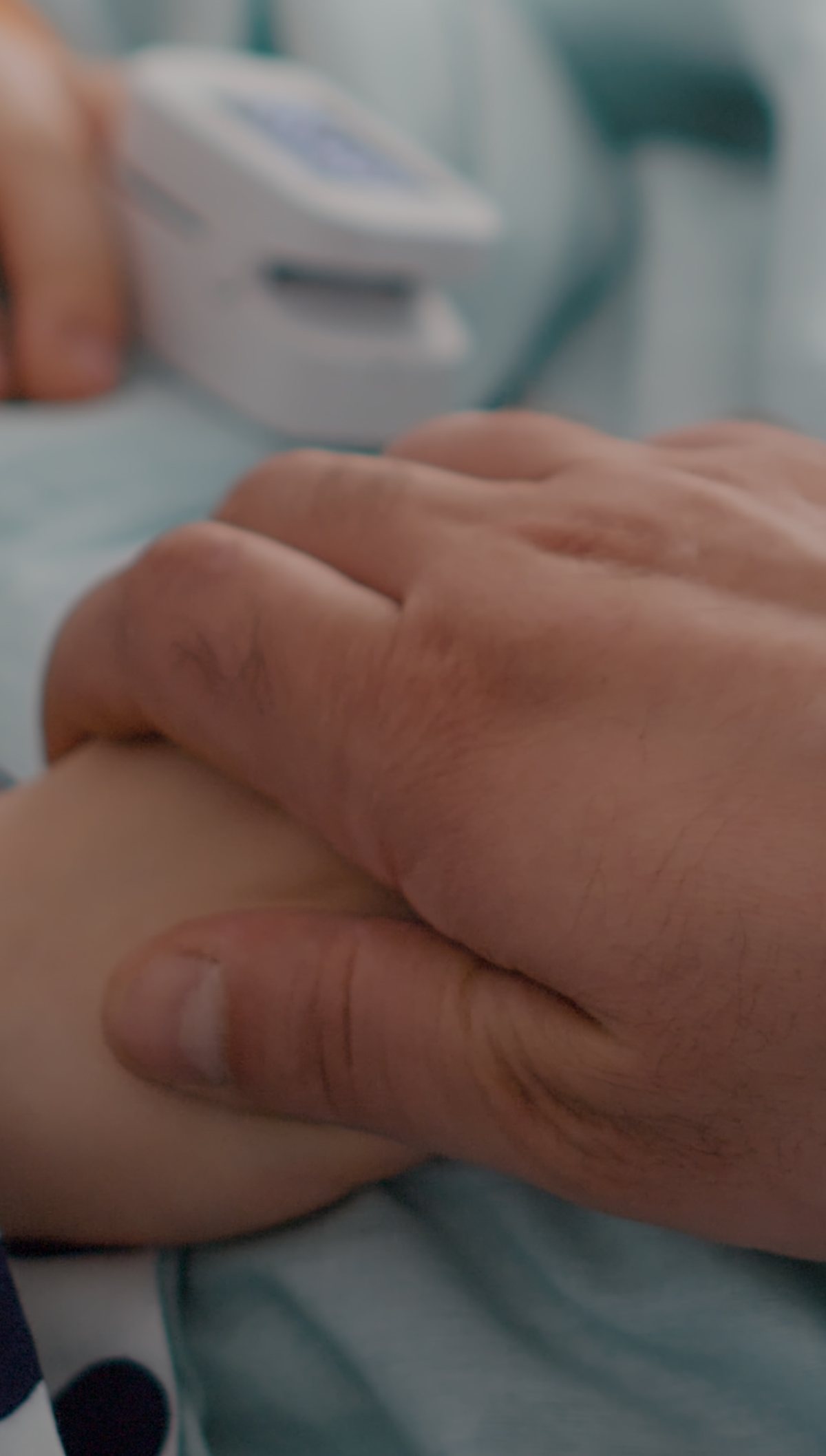 An adult holding the hand of a child resting in a hospital bed